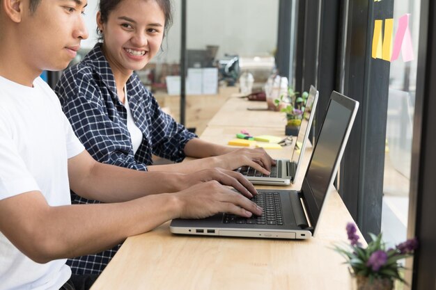 Foto vista lateral de un hombre y una mujer usando una computadora portátil mientras están sentados en la mesa