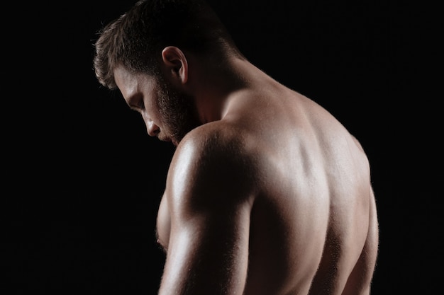 Vista lateral del hombre musculoso desnudo. fondo oscuro aislado