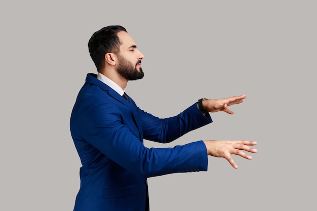 Vista lateral del hombre de negocios barbudo caminando con los ojos cerrados y extendiendo las manos para encontrar el camino