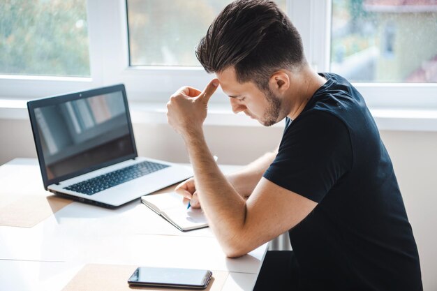 Vista lateral de un hombre de negocios escribiendo algo en su cuaderno usando un teléfono móvil inteligente mientras trabaja ...