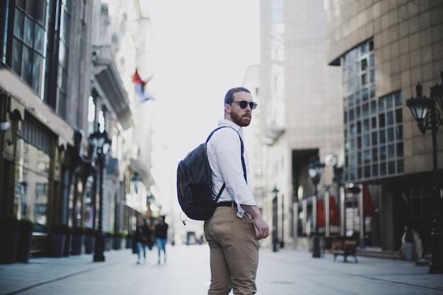 Vista lateral de un hombre de negocios con una mochila de pie en la calle de la ciudad