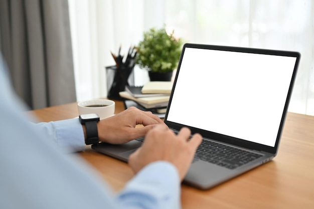 Vista lateral del hombre de negocios que usa una computadora portátil en un escritorio de oficina de madera Pantalla blanca vacía para su publicidad y diseño creativo