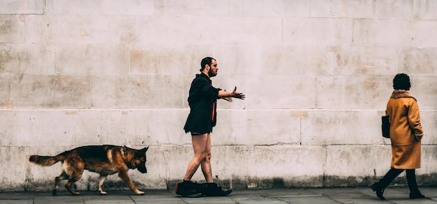 Vista lateral de un hombre con los pantalones bajados caminando por un perro y una mujer contra la pared