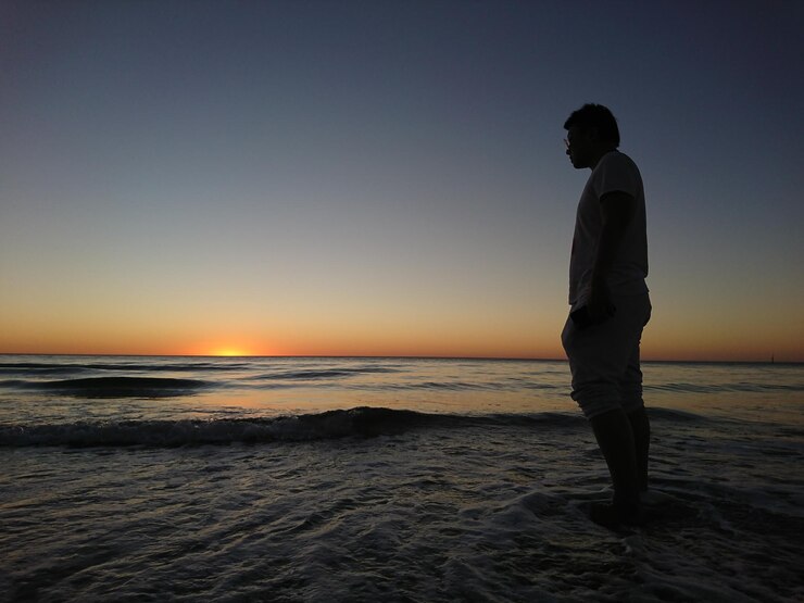 Foto vista lateral de un hombre de pie en la playa contra un cielo despejado durante la puesta de sol