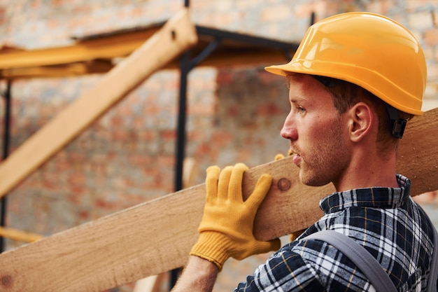 Vista lateral del hombre que sostiene tablas de madera Trabajador de la construcción en uniforme y equipo de seguridad tiene trabajo en la construcción