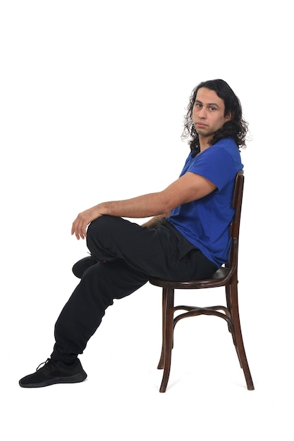 vista lateral de un hombre con ropa deportiva sentado en una silla mirando a la cámara sobre fondo blanco