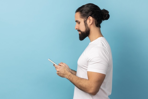 Vista lateral de un hombre serio y atractivo que usa un teléfono móvil mirando el mensaje de escritura de la pantalla del dispositivo