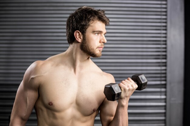 Vista lateral del hombre serio que levanta el peso en el gimnasio