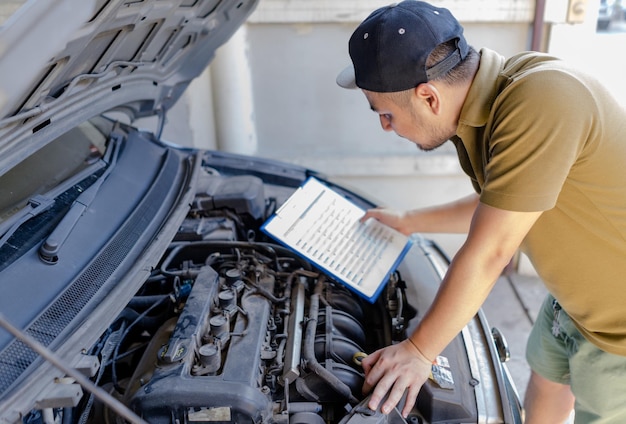 Vista lateral de un hombre sosteniendo una lista de comprobación mientras mira el motor del automóvil