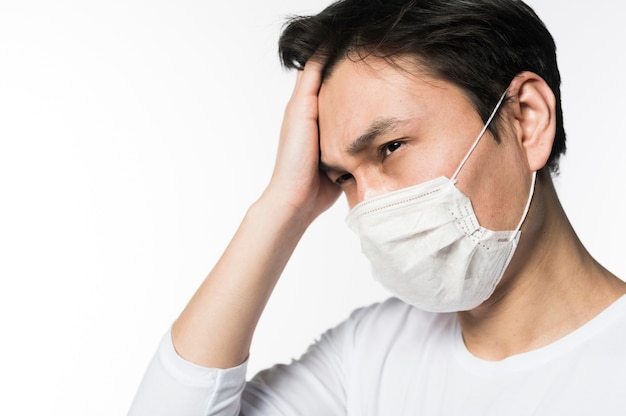 Foto vista lateral del hombre triste tocando su cabeza mientras usa una máscara médica