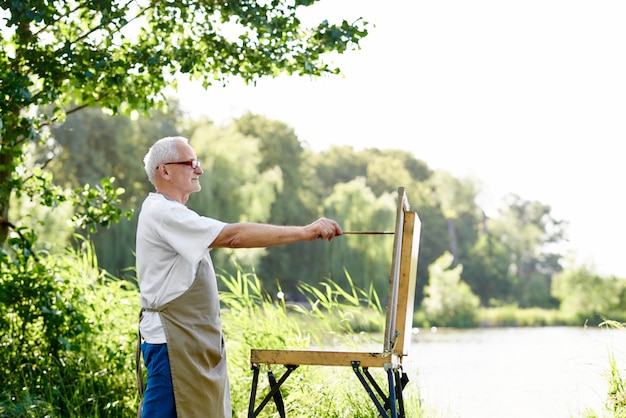 Vista lateral de la imagen masculina hermosa del dibujo del pintor en el d3ia en el parque contra el lago.