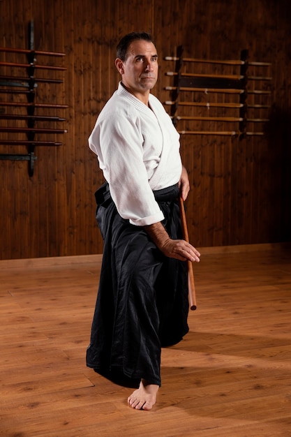 Foto vista lateral del instructor de artes marciales masculino en la sala de práctica con palo de madera