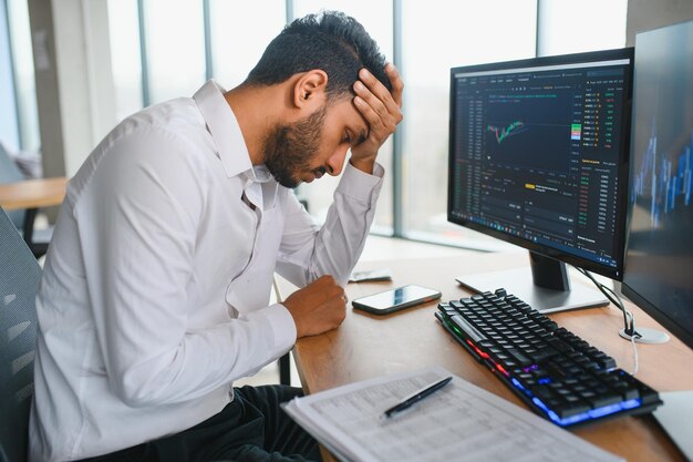 Vista lateral de un inteligente corredor de analistas de inversores criptográficos indios que usa una computadora portátil y un teléfono inteligente que analiza los gráficos del mercado de valores de intercambio digital de criptomonedas pensando en los riesgos de inversión y fondos