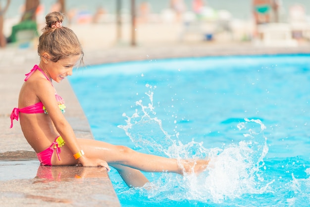 Vista lateral irmãzinhas nadando na piscina e jogando água umas nas outras durante as férias