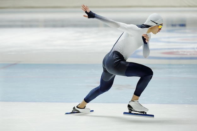 Vista lateral del joven activo en uniforme deportivo practicando ejercicios en la pista de hielo