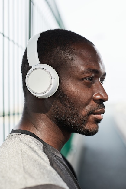 Vista lateral del joven africano en auriculares inalámbricos escuchando música mientras está de pie al aire libre