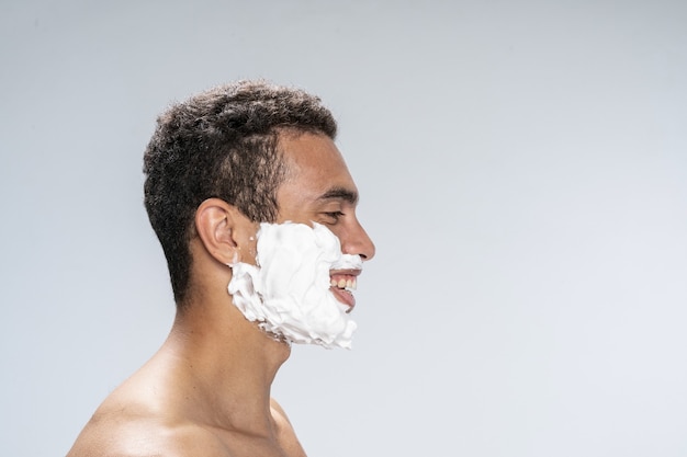 Vista lateral de un joven alegre con espuma de afeitar en el rostro