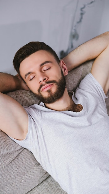 Vista lateral de un joven apuesto hombre barbudo con ropa informal duerme o se relaja en el sofá en una habitación en casa