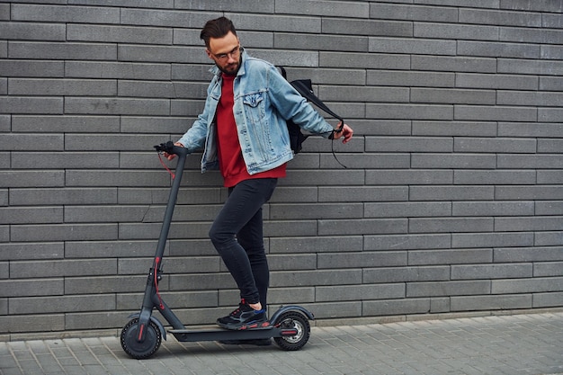 Vista lateral de un joven apuesto con ropa informal que monta una moto eléctrica al aire libre durante el día soleado