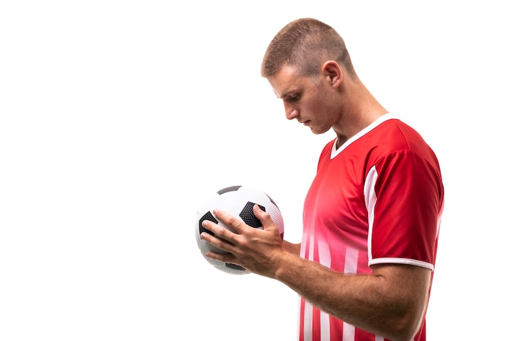 Foto vista lateral de un joven atleta caucásico mirando una pelota de fútbol sobre un fondo blanco