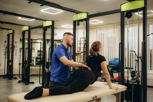 Foto vista lateral de una joven atleta haciendo ejercicios de flexión de la espalda durante la fisioterapia después de una lesión deportiva especialista del centro de salud ayudando a la mujer a recuperar la flexibilidad de la espaldas después de un trauma