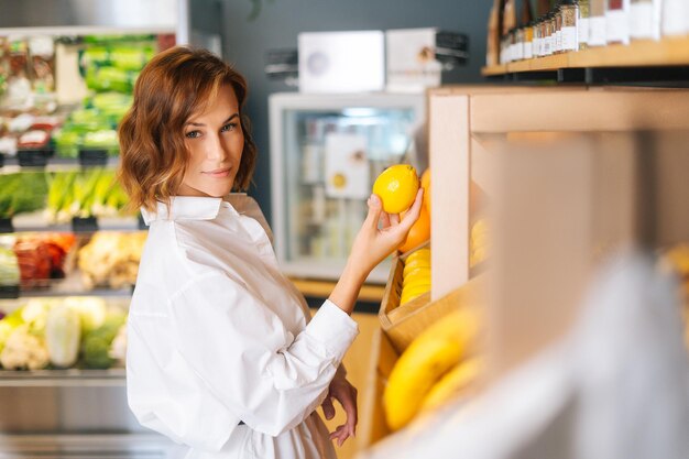 Vista lateral de la joven y bonita elección de frutas para la dieta de control de limón en la tienda de comestibles en el