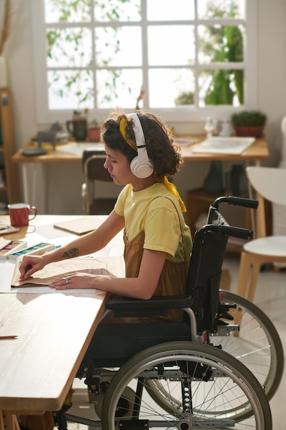 Foto vista lateral de una joven creativa en silla de ruedas dibujando con crayones