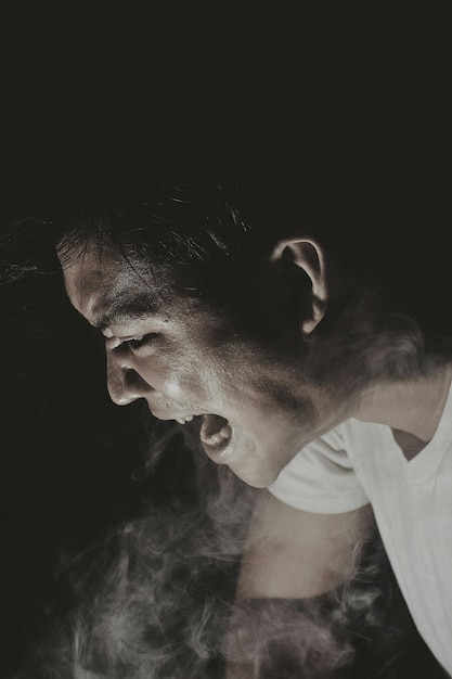 Vista lateral de un joven enojado emitiendo humo contra un fondo negro