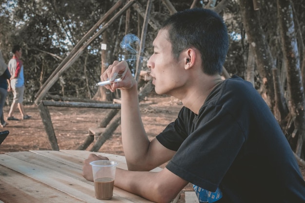 Vista lateral de un joven fumando un cigarrillo mientras está sentado en el parque