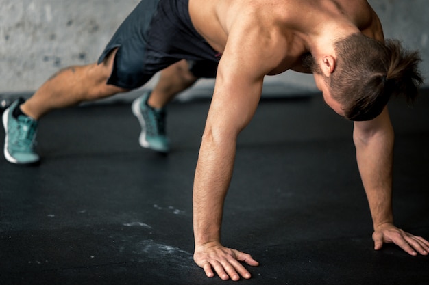 Vista lateral del joven guapo en ropa deportiva haciendo flexiones en el gimnasio