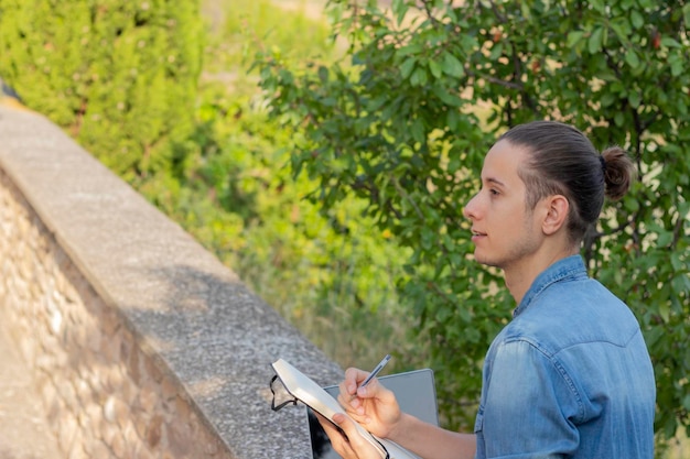 Vista lateral del joven hipster mirando hacia un lado y dibujando como actividad de pasatiempo en la naturaleza