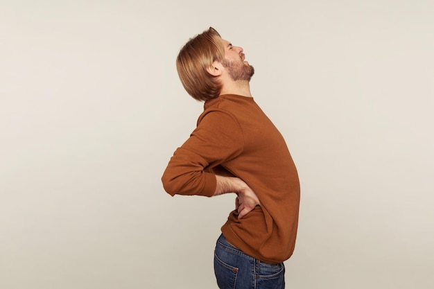 Vista lateral de un joven malsano que sufre un dolor agudo y repentino en el disco de la columna vertebral lesionado en la parte baja de la espalda o en un nervio pellizcado