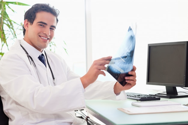 Vista lateral del joven médico en su escritorio con una radiografía