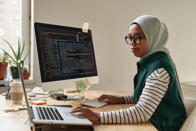 Vista lateral de un joven pasante o desarrollador de software profesional que toca el panel táctil de la computadora portátil mientras mira