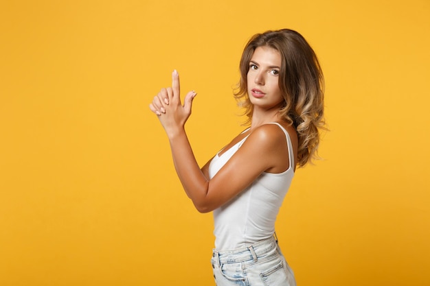 Vista lateral de una joven segura de sí misma con ropa informal ligera posando aislada en un fondo de pared naranja amarillo, retrato de estudio. Concepto de estilo de vida de las personas. Simulacros de espacio de copia. Tomados de la mano como un arma.