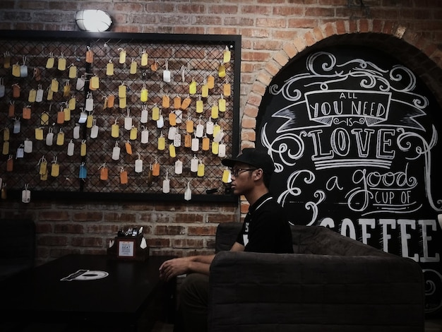Foto vista lateral de un joven sentado junto a la pared en una cafetería