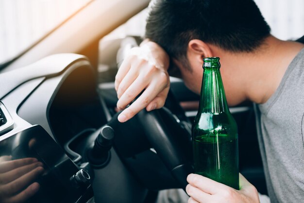 Foto vista lateral de un joven sosteniendo una botella de cerveza mientras está sentado en el coche