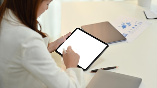 Vista lateral de una joven trabajadora de oficina usando un lápiz óptico escribiendo en la pantalla de una tableta digital en blanco