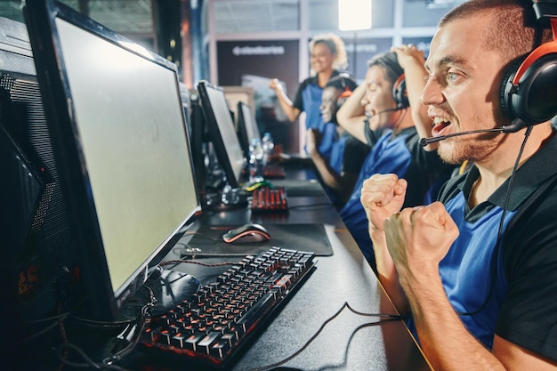 Foto vista lateral de los jugadores cibernéticos profesionales entusiasmados, el equipo multirracial de deportes cibernéticos que celebra el éxito mientras juegan videojuegos en línea, participan en un torneo o competencia de esports