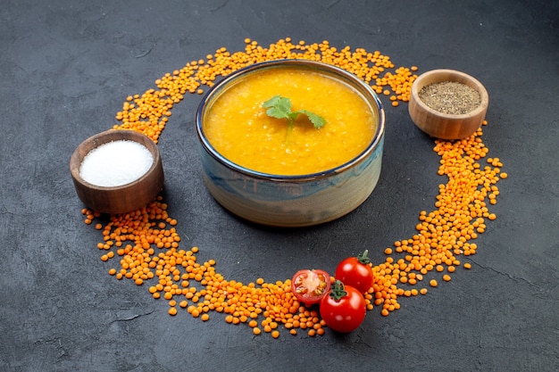 Vista lateral de lentejas rojas alineadas en un círculo y deliciosa sopa de sal de pimienta sobre fondo negro con espacio libre