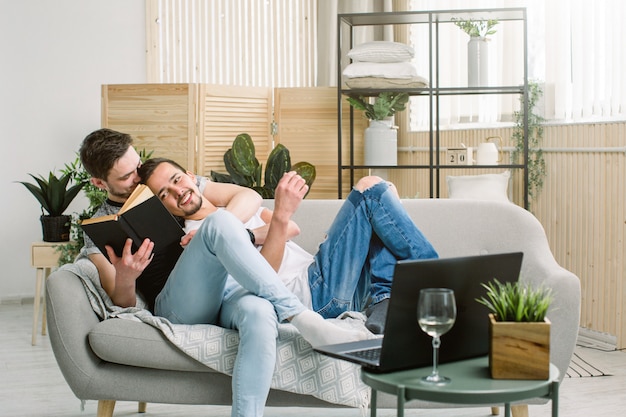 Vista lateral de un libro de lectura relajado joven pareja gay en el sofá en casa