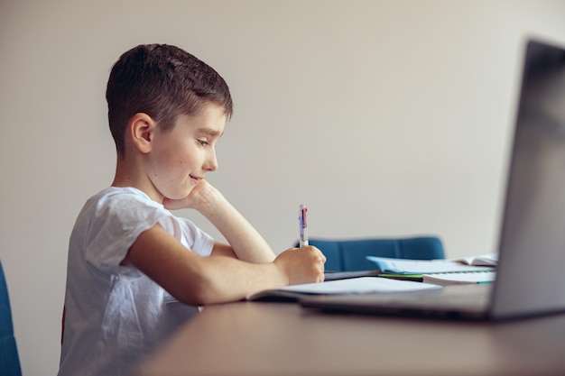 Vista lateral del lindo alumno de niño pequeño con aparatos ortopédicos escribiendo ejercicio en cuaderno y sonriendo