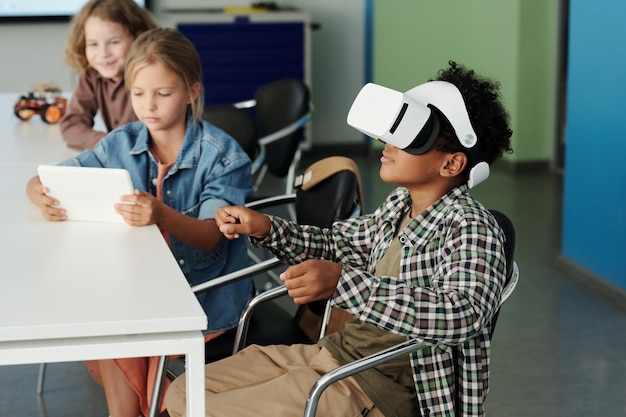 Foto vista lateral del lindo colegial afroamericano en robot de control de auriculares vr