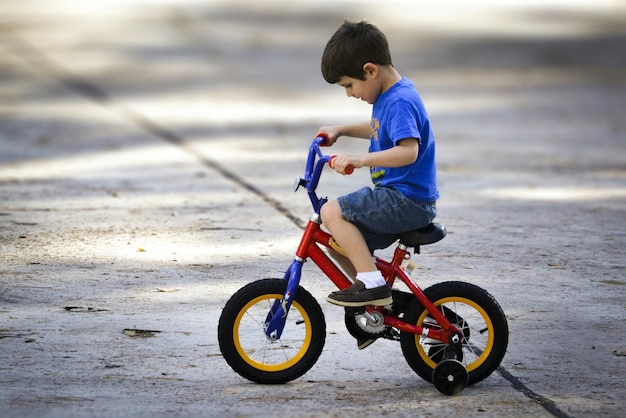 Vista lateral de longitud completa de un niño montando una bicicleta en la calle