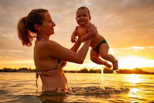 Vista lateral de la madre feliz con pequeño niño sonriente lindo sobre agua de mar caliente