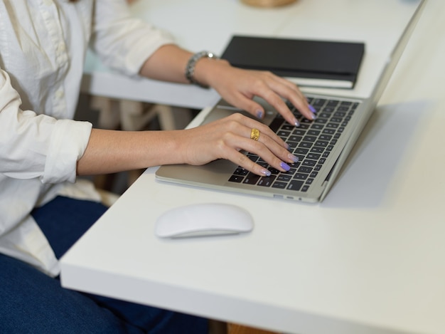 Foto vista lateral de la mano femenina escribiendo en el teclado del portátil en el escritorio de oficina blanco