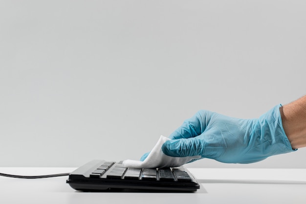 Foto vista lateral de la mano con guante quirúrgico que desinfecta el teclado con espacio de copia