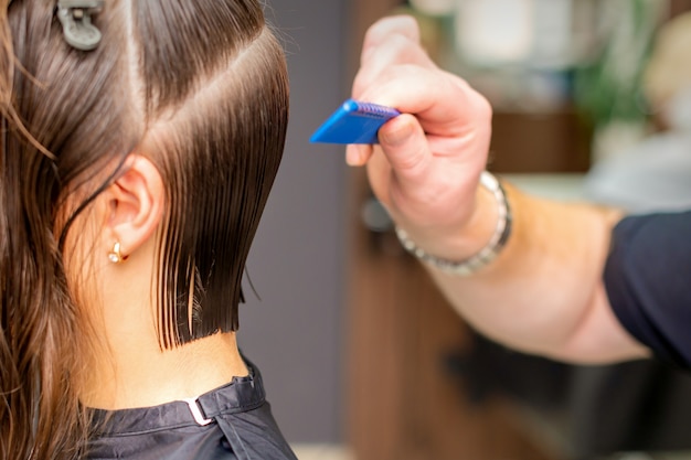 Vista lateral de la mano del peluquero haciendo corte de pelo de mujer joven por peine en peluquería