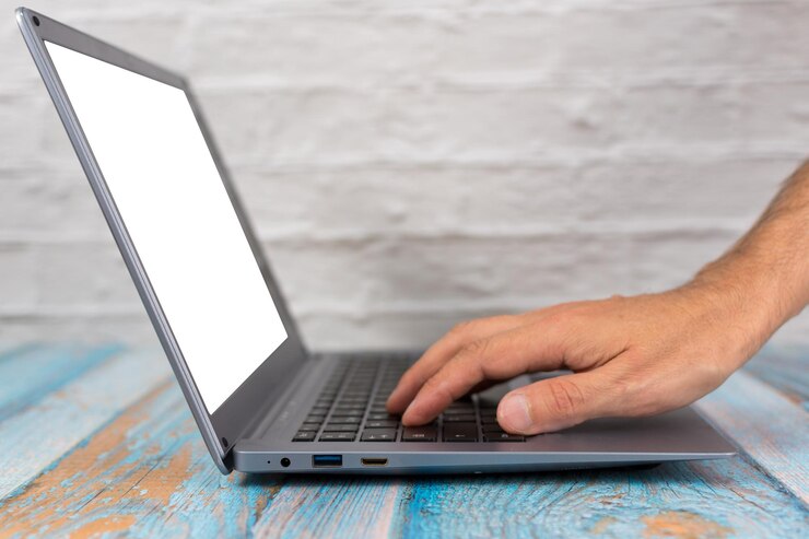 Foto vista lateral de una mano en el teclado de una computadora portátil con una pantalla en blanco