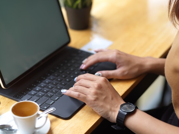 Vista lateral de manos femeninas escribiendo en el teclado de la tableta mientras trabaja en la cafetería